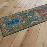 A long runner rug with a distressed traditional pattern in teal, blue, papaya, and honey, laid out diagonally on a light-colored wooden plank floor.