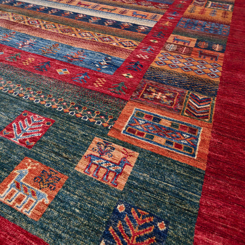 A close-up of a hand-woven Afghan rug with a geometric pattern in red, blue, orange, and green, featuring stylised animal motifs.