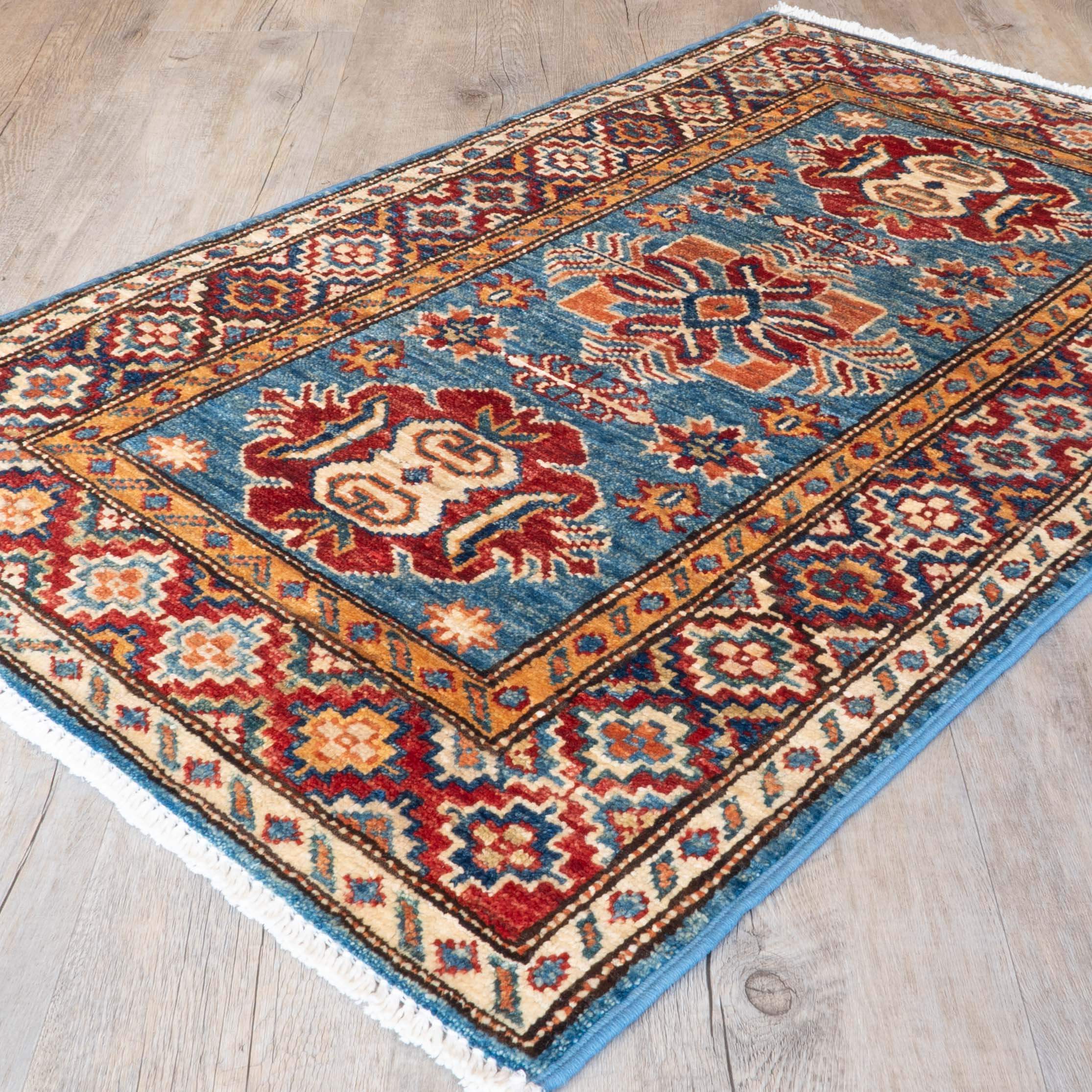A traditional Persian-style area rug with a blue field, red and beige medallions, and a patterned border, shown on a light wood floor.