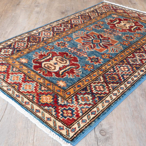 A traditional Persian-style area rug with a blue field, red and beige medallions, and a patterned border, shown on a light wood floor.