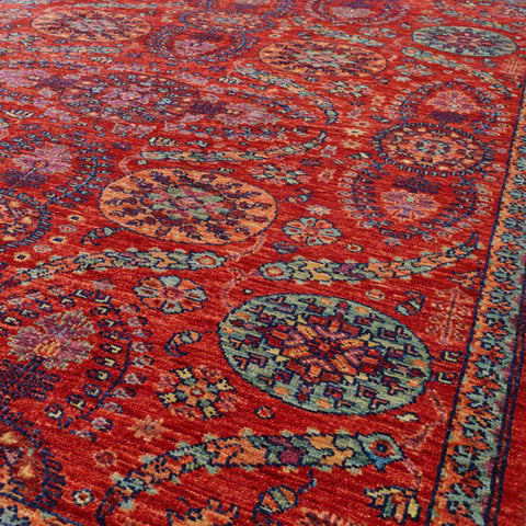 A close-up view of a traditional patterned area rug with a vibrant red base and intricate medallion motifs in peach, green and heather.