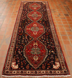 A deep blue ground holds 4 connected leaf shapes in the main area going through the length, these are in broght red.  There is a border in cream. In each corner there is a horses head in cream.  All over, all areas of this rug are depictions of flowers, birds and butterflies. 