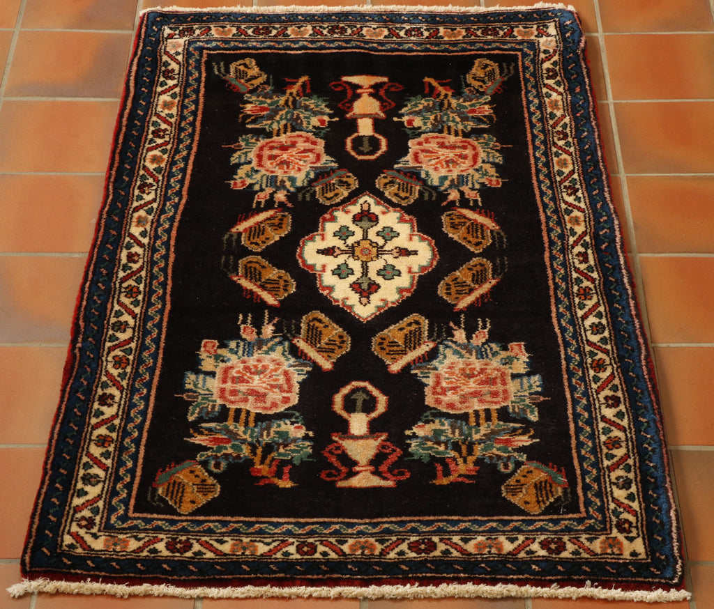 This small mat has a bold design laid upon a dark blue ground.  The main medallion in the centre with a small floral pattern within it.  Beyond it there are a series of butterflies in gold, with black and red highlights.  In each corner can be found a leaf and flower design in cream, pink, blue and green.  There are three narrow borders two with deep blue grounds and the central one cream.  