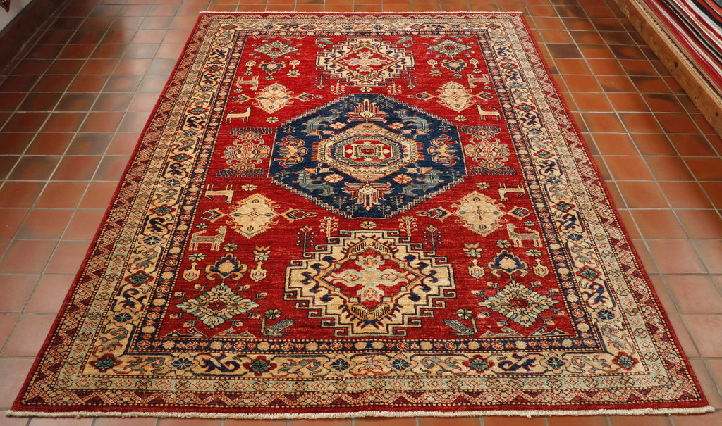 Blue central decorative medallion in the centre of the rug with two smaller ones at either end in cream.  This is all on a tomato red background.  There are 4 inner borders of differing widths and designs.  