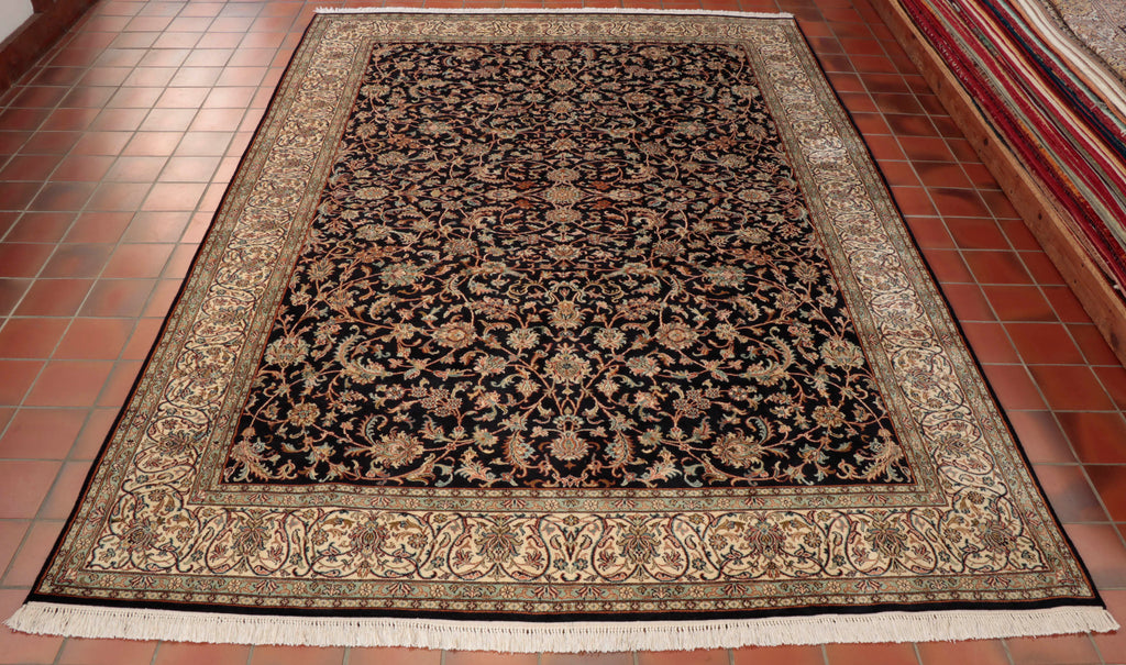 This Kashmir carpet has an intricate Persian floral design. It has been hand knotted in Kashmir using silk for the pile and cotton for the warp and weft. The background colour is a very dark navy blue and the border is ivory. Other  colours used are rust, olive green, rose pink and duck egg blue.