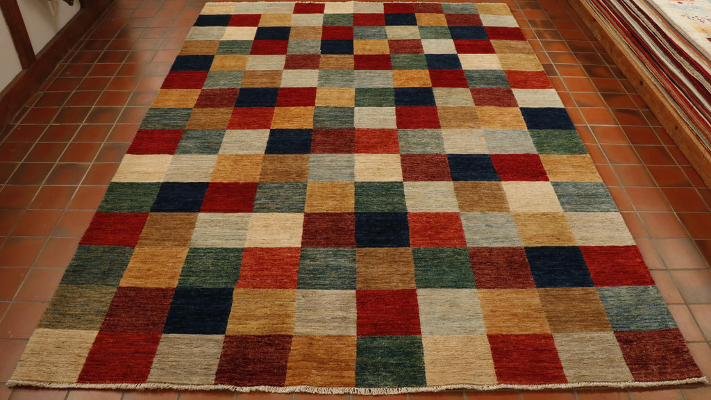 Chequerboard rug throughout the piece squares of colour.   The colour palette consists of oatmeal, red, brown, golden yellow, sea green, cream, sea blue, olive green, orange and dark blue.  10 squares across the width by 15 through the length. 