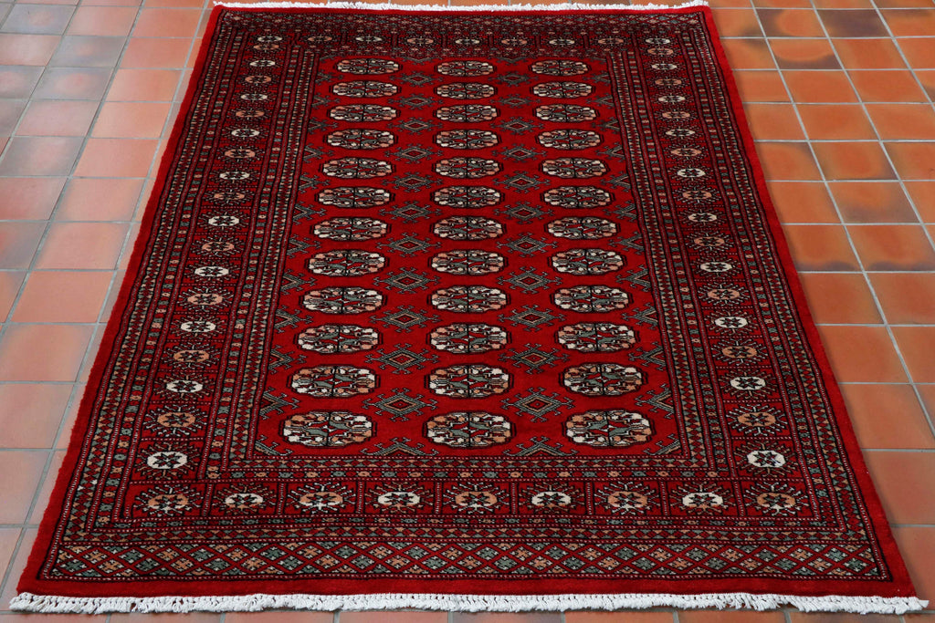 A deep red ground with a green, peach and cream pattern design with the highlights for the pattern work being in black.  The design is a standard classic Bokhara design.  