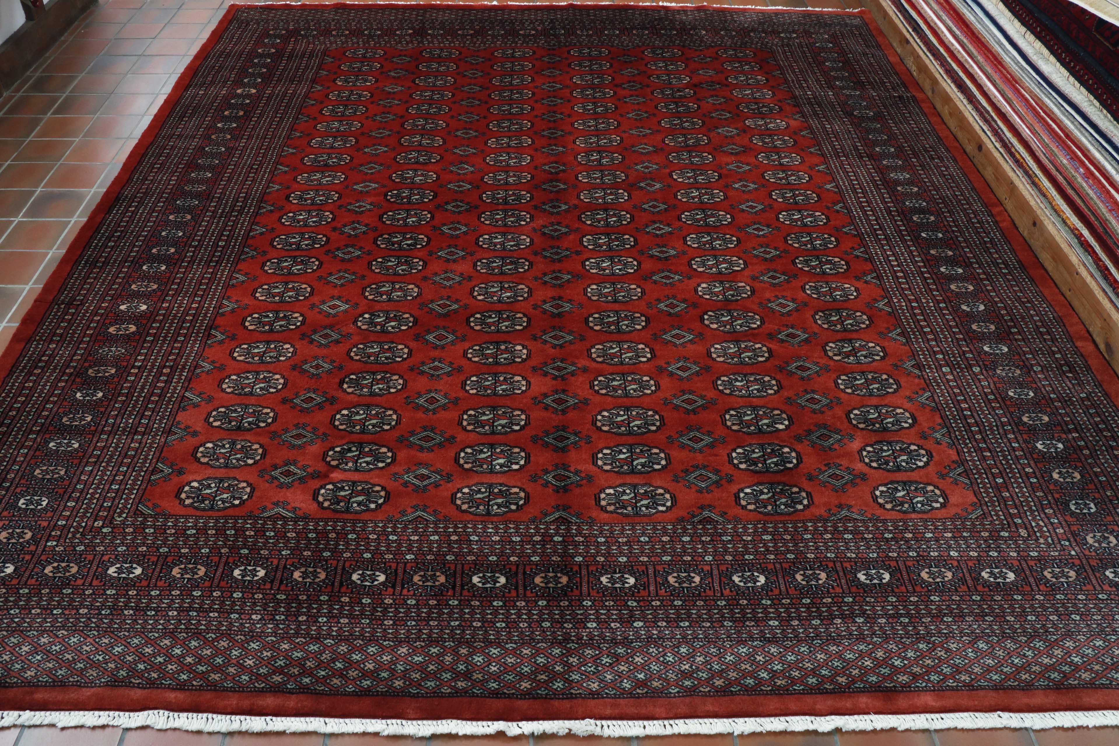 This Bokhara has a rich red ground with bands of stylized flowers, 6 bands in total across the length of the piece.   These are outlined in very dark blue/black with the inner pattern uses a soft peach, soft duck egg blue/green and cream as highlights.   There is a broad band of border, made up of several different width sized areas of smaller border using the same colour palette.  These are decorated in small and large flower designs and the broader outer border being a trellis decoration. 