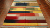  This Indian kilim has bands of blended colours across the horizontal.  The bands have the colour palette of yellow, reds, dark blue, light blue, greens, orange, turquoise, grey and cream.  The bands are of varying widths. 