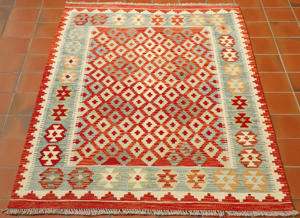 A simple repeating diamond is used in the centre-ground of this kilim. The diamonds are cream soft blue and sage green which contrasts well against the red/orange. the inner border is also a seagrass blue-green.