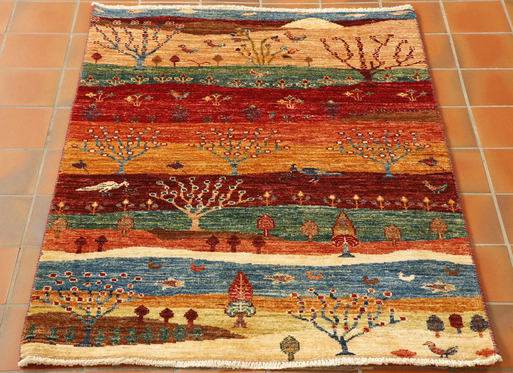 The piece is a rural scene with many colours, including blue, green, red, and orange.  There are many plants, trees and birds, in particular two lovely peacocks. 